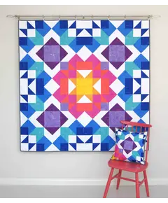 Aurora Quilt Pattern by Tied With A Ribbon - Quilt hung on wall and pillow resting on a chair