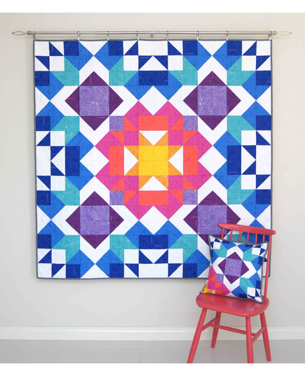 Aurora Quilt Pattern by Tied With A Ribbon - Quilt hung on wall and pillow resting on a chair