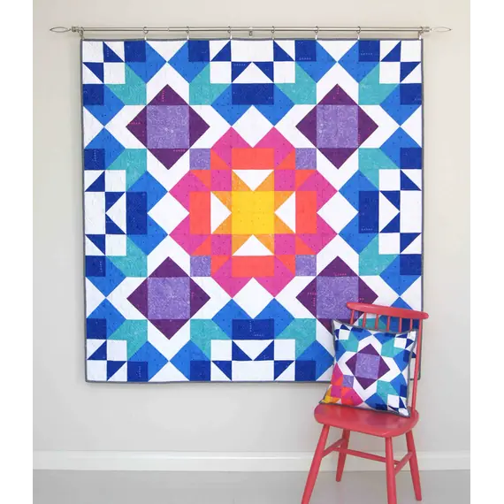 Aurora Quilt Pattern by Tied With A Ribbon - Quilt hung on wall and pillow resting on a chair